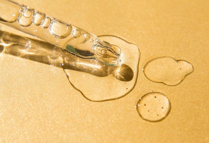 Glass dropper with clear liquid on a gold background